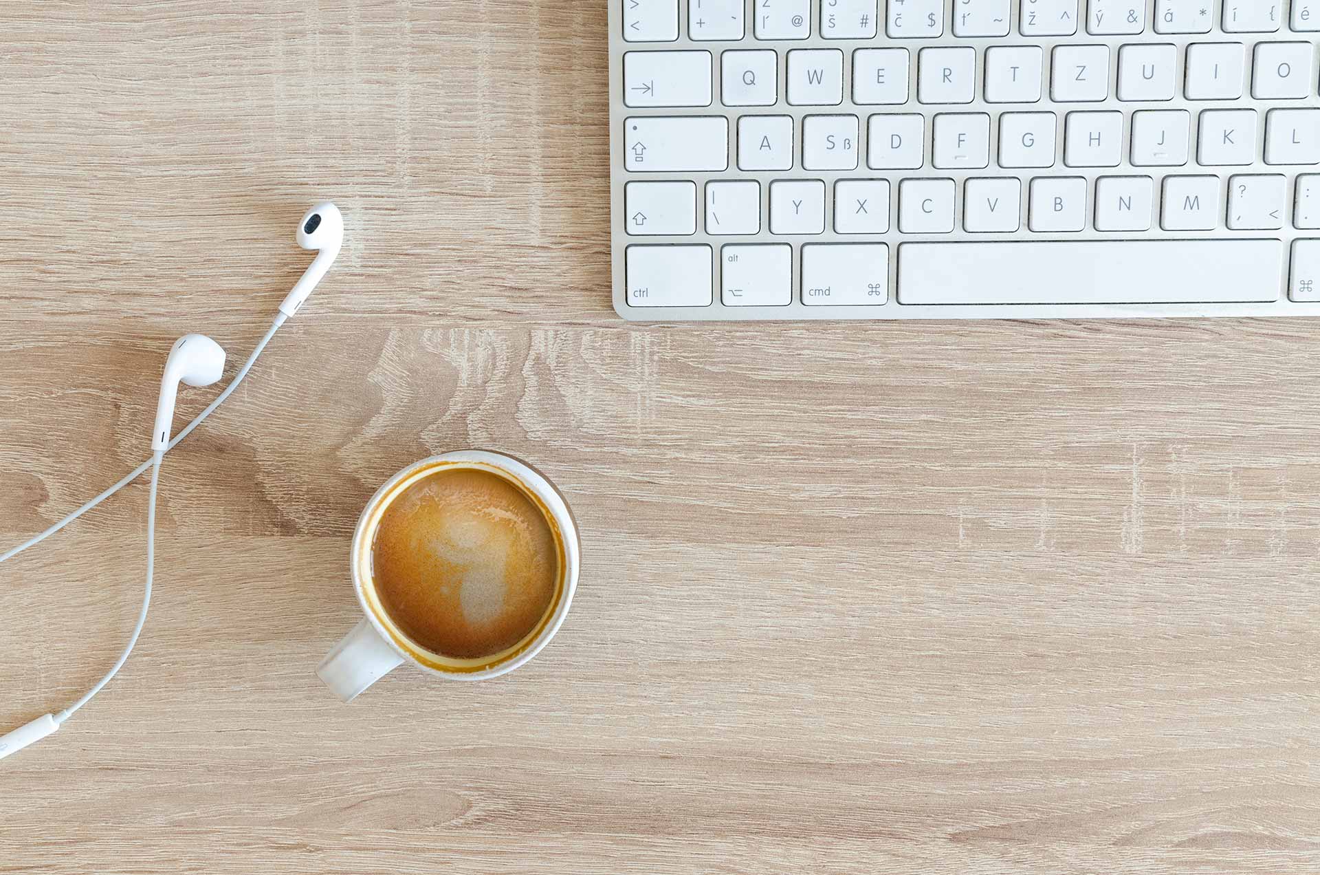 Top-down view of desk with laptop, earbuds and coffee